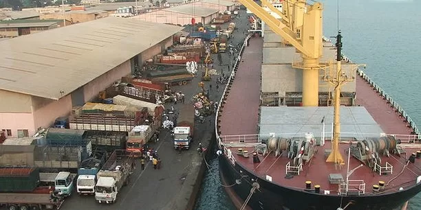Vue aérienne d’un port avec un grand cargo amarré à quai et plusieurs camions stationnés le long du déchargement