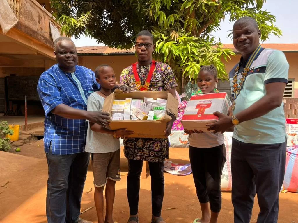 Quatre personnes et deux enfants debout dehors tenant des boîtes de fournitures alimentaires et de soins sous un arbre