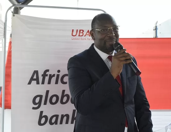 Un homme en costume sombre parle dans un micro devant une bannière avec le texte partiel UBA Africa global bank