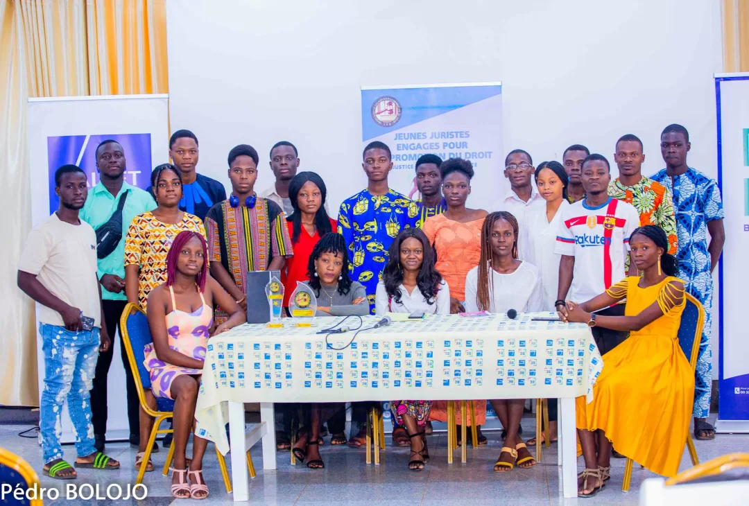Un groupe de jeunes vêtus de tenues variées posant autour d’une table avec des trophées et des affiches en arrière-plan