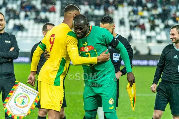 Deux joueurs de football s’embrassent sur le terrain avant le coup d’envoi sous le regard des arbitres et d’autres joueurs