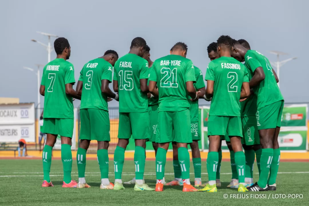 Joueurs de football en cercle bras dessus bras dessous en maillot vert sur un terrain de football