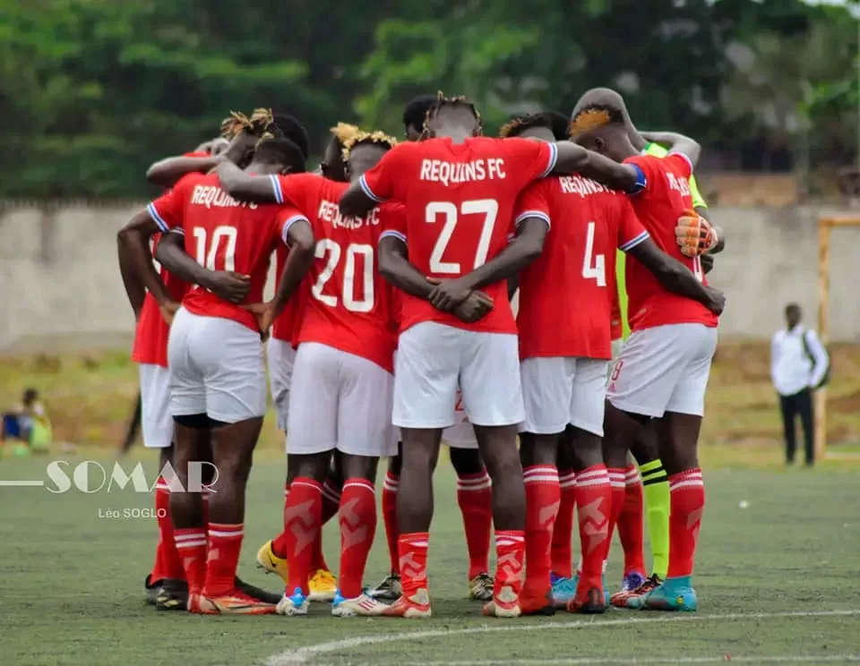 Joueurs en maillot rouge formant un cercle de cohésion sur un terrain de football gazonné