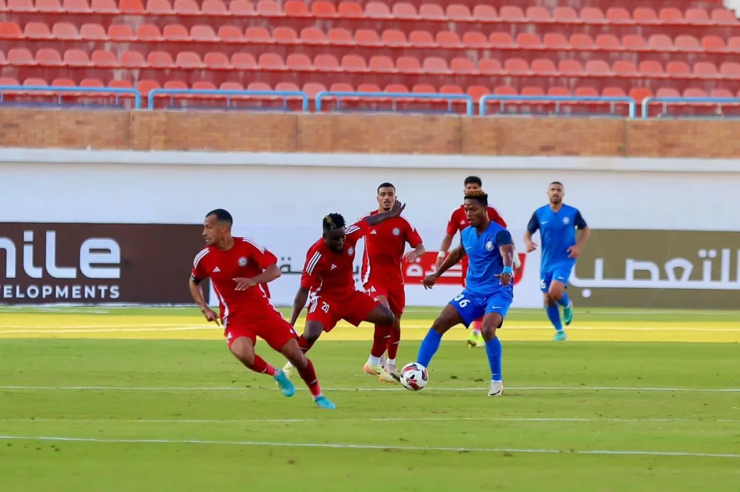 Joueurs en action sur un terrain de football, l’un en bleu contrôle le ballon, plusieurs adversaires en rouge tentent de l’intercepter