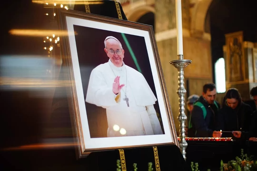 Portrait encadré d un homme en tenue blanche avec une croix, posé sur un lutrin près d une grande bougie allumée
