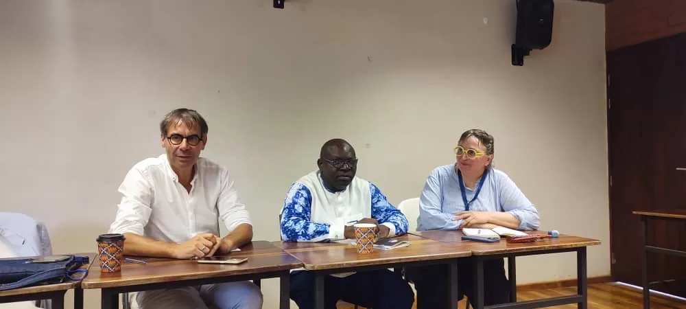 Trois personnes assises à une table face au public dans une salle de conférence avec mic et gobelets colorés.