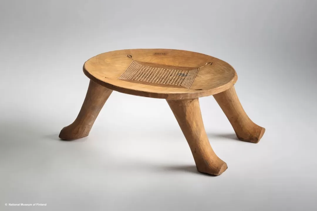 Tabouret en bois clair avec un plateau circulaire orné d'une gravure quadrillée et quatre pieds courbés vers l'extérieur
