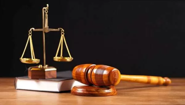 Balance de justice dorée posée sur un livre à côté d’un marteau en bois sur une table en bois