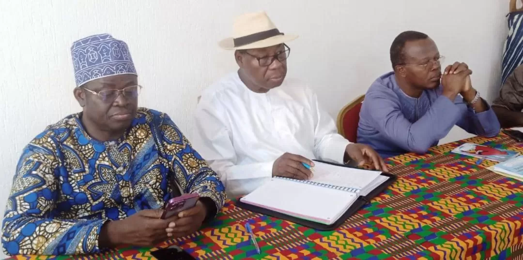 Trois hommes assis à une table colorée consultent un carnet et un téléphone portable dans une réunion.