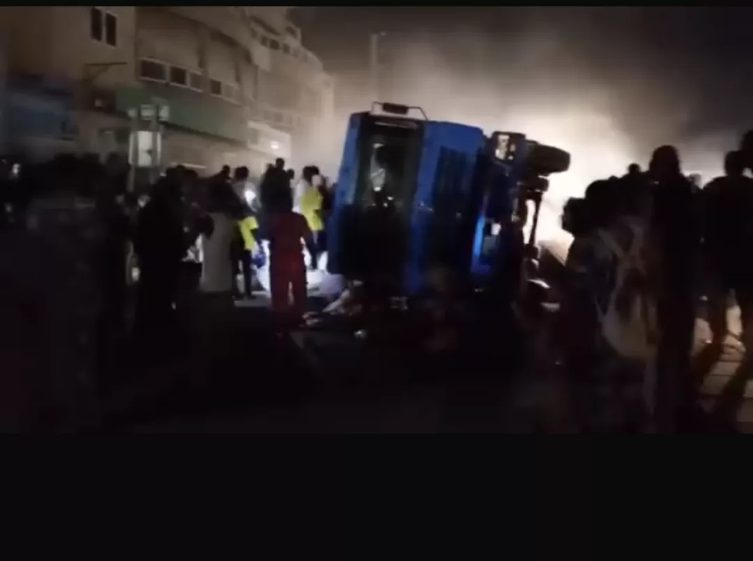 Camion renversé sur le côté entouré de plusieurs personnes dans une rue obscure éclairée par des phares