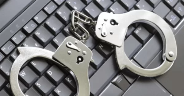 Menottes posées sur un clavier d’ordinateur noir symbolisant la cybercriminalité