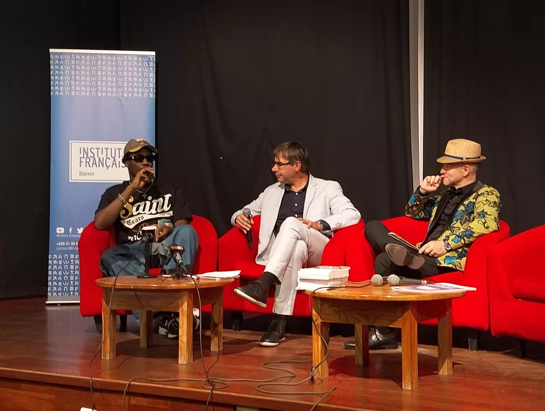 Trois hommes assis sur des fauteuils rouges participent à une discussion sur scène devant une bannière Institut Français