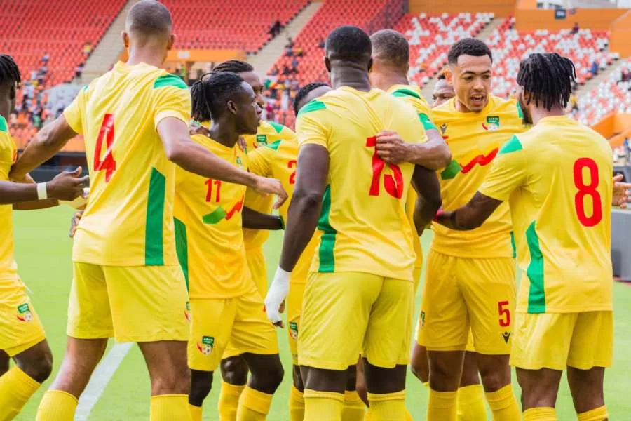 Dix joueurs en maillot jaune avec des motifs rouges et verts se rassemblent sur un terrain de football en stade quasi vide