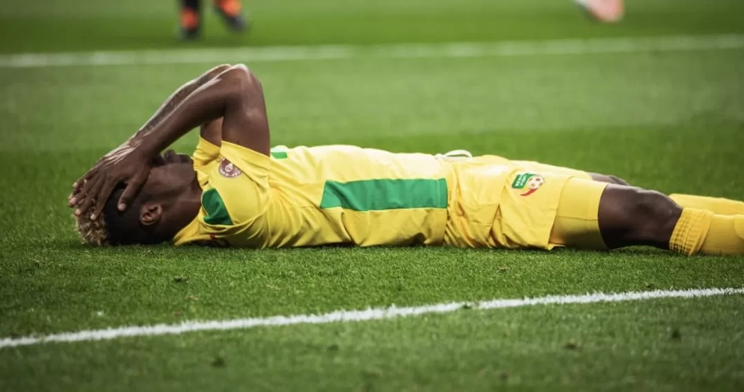 Un joueur de football allongé sur le terrain, les mains sur la tête, semblant déçu ou fatigué