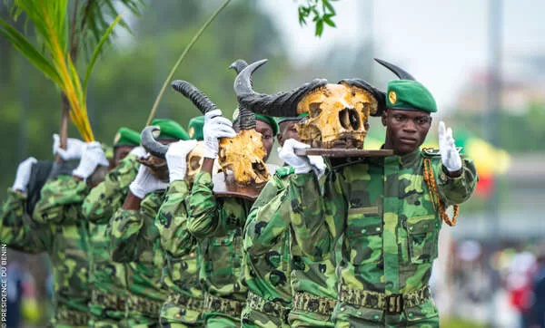 Des militaires en uniforme camouflé et béret vert portent des crânes d'animaux à cornes lors d'une cérémonie en extérieur
