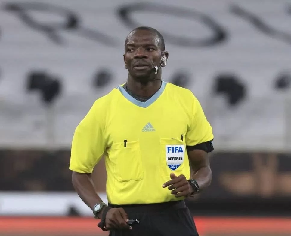 Arbitre en tenue jaune avec badge FIFA en train d'observer le jeu durant un match de football