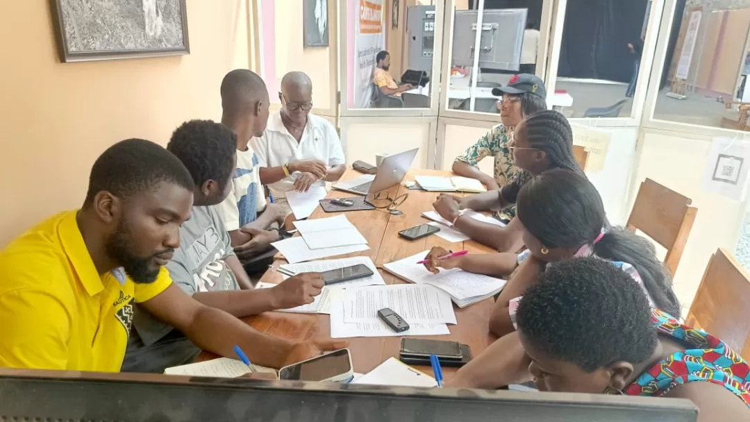 Plusieurs personnes assises autour d’une table en bois en réunion avec documents et ordinateurs portables.