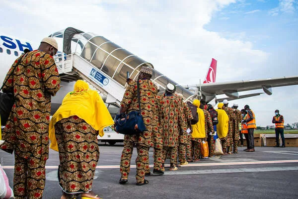 Une file de passagers vêtus de tenues assorties monte à bord d’un avion par une passerelle extérieure sur le tarmac