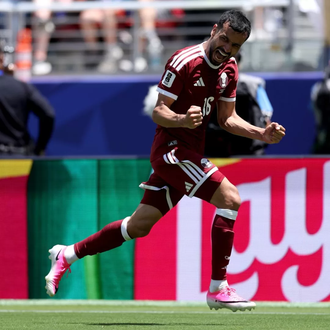 Joueur en maillot rouge foncé célèbre un but en serrant les poings sur un terrain de football en plein jour