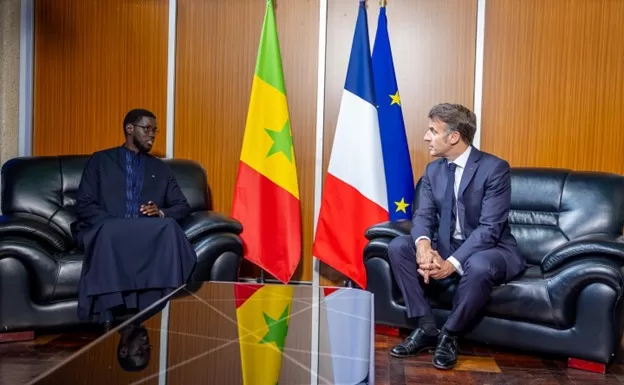 Deux hommes assis face à face dans un bureau avec les drapeaux du Sénégal et de la France entre eux