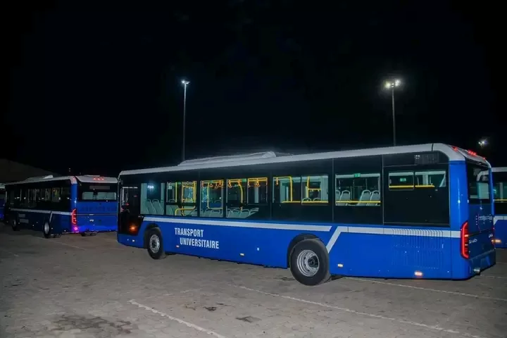 Deux bus bleus immobiles sur un parking éclairé la nuit avec l'inscription "TRANSPORT UNIVERSITAIRE" sur le côté