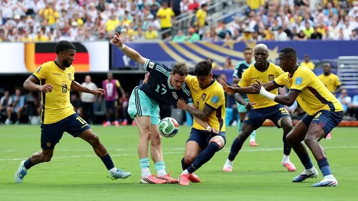 Un joueur en maillot vert clair entouré de plusieurs adversaires en maillot jaune lutte pour le ballon sur un terrain de football.