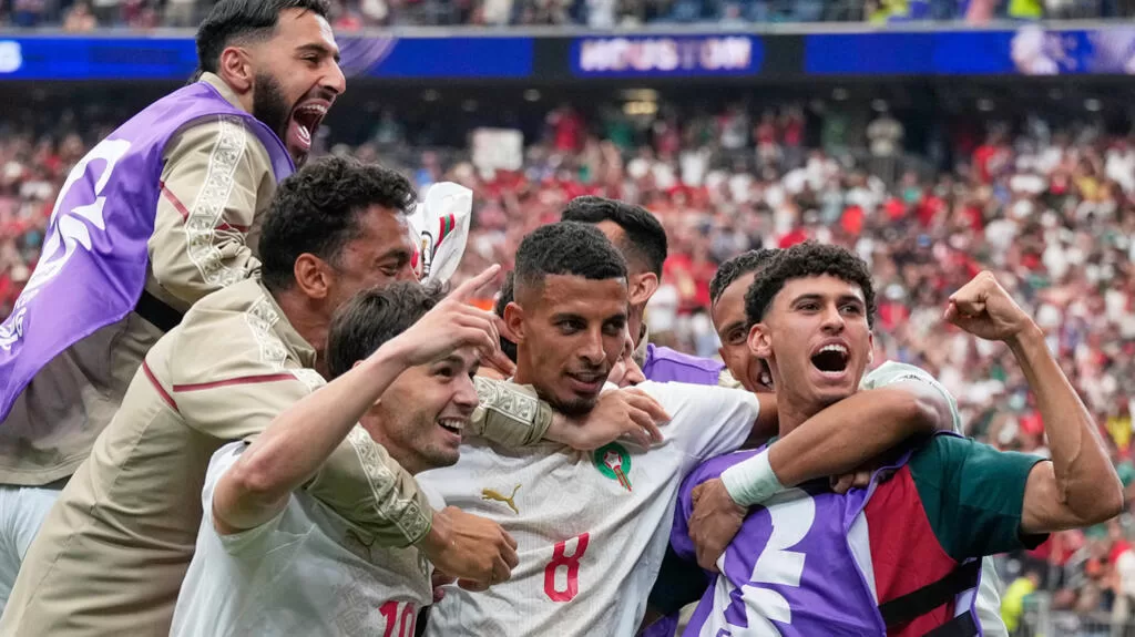 Groupe de joueurs de football en maillots blancs célébrant joyeusement un but dans un stade rempli de supporters