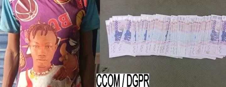 Un homme tenant un faux billet à côté d'une rangée de billets de banque de 1000 FCFA posés sur une surface grise