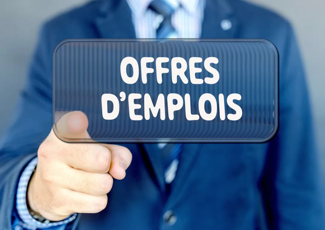 Un homme en costume pointe vers un panneau transparent avec le texte OFFRES D’EMPLOIS en blanc