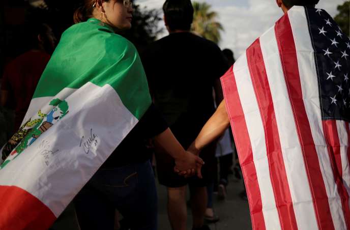 Deux personnes marchent main dans la main, drapées des drapeaux mexicain et américain en extérieur