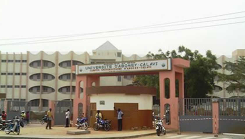 Façade d’un bâtiment universitaire avec portail d’entrée et plusieurs personnes à pied et à moto devant