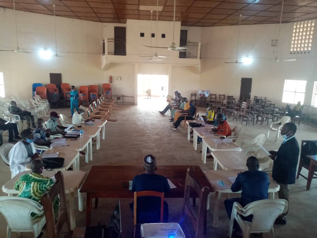 Personnes assises autour de tables en U dans une grande salle pour une réunion dans le respect des distances sociales