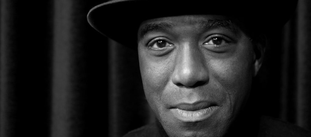 Portrait en noir et blanc d’un homme portant un chapeau et regardant la caméra avec une légère expression souriante