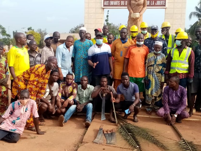 Un groupe d'hommes posant devant une statue avec des outils de nettoyage et de jardinage au sol