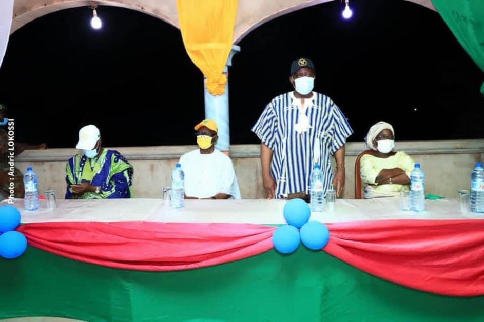 Quatre personnes assises derrière une table décorée aux couleurs vives sous un ciel nocturne avec masques et bouteilles d'eau devant elles