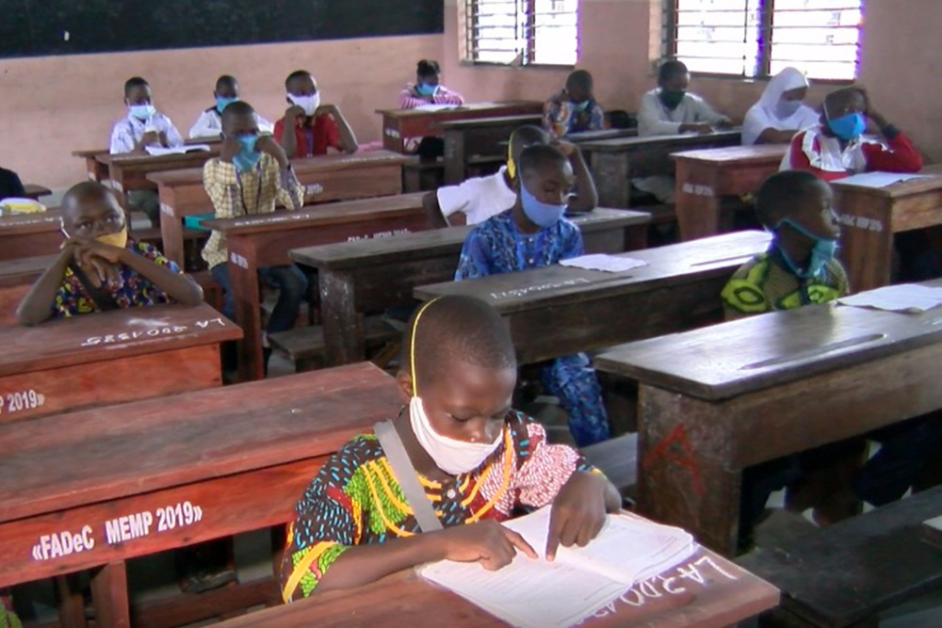 Des élèves masqués sont assis à des bureaux en bois dans une salle de classe durant un examen