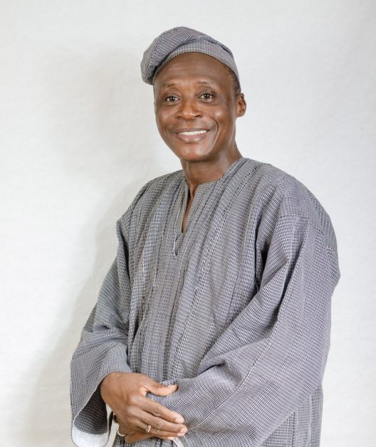 Homme souriant vêtu d’une tenue traditionnelle à carreaux et coiffé d’un bonnet assorti sur un fond clair