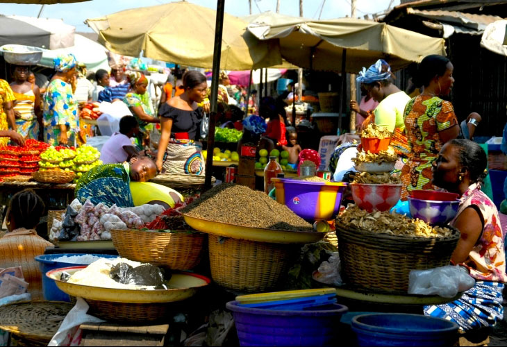 Marché animé avec des vendeuses en tenues colorées proposant divers produits alimentaires dans des paniers et bassines