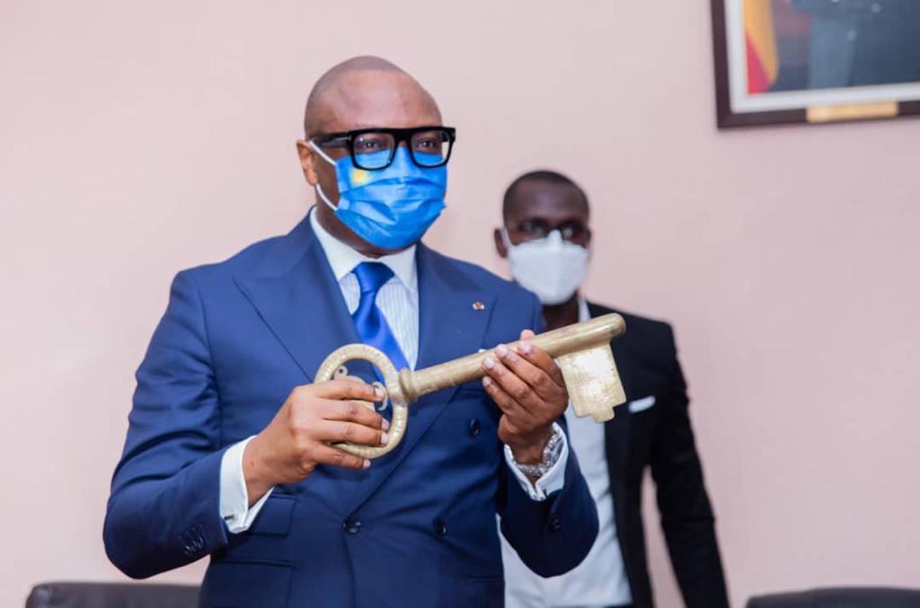 Un homme en costume bleu et masque tient une grande clé dorée avec une autre personne masquée en arrière-plan
