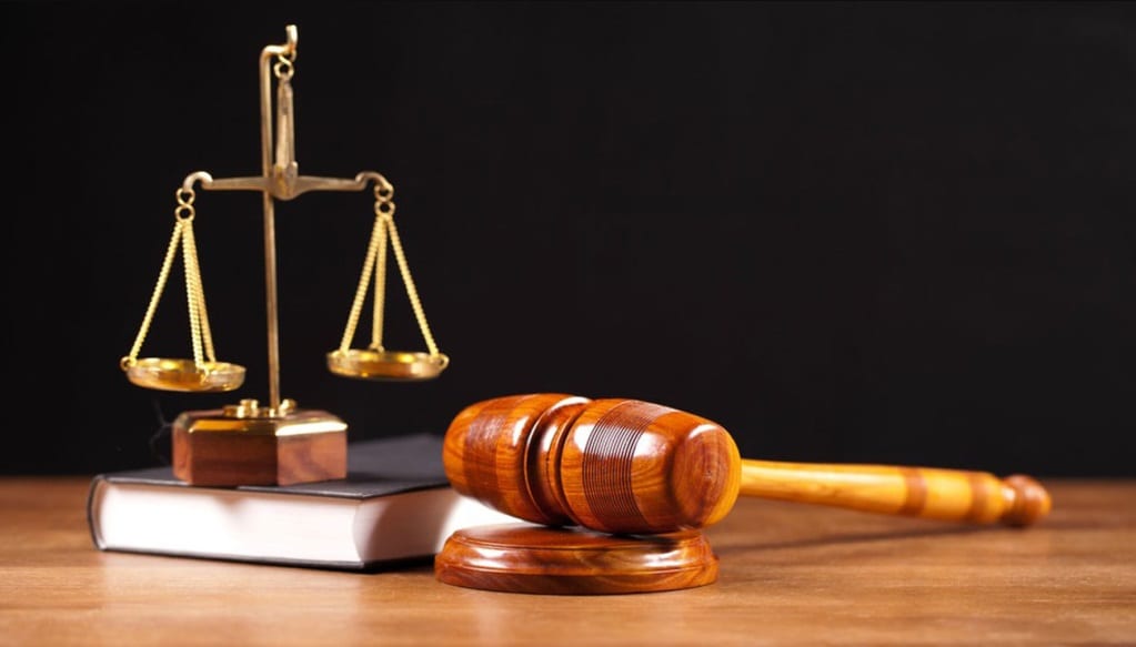 Balance de justice dorée posée sur un livre à côté d un marteau en bois sur une table en bois