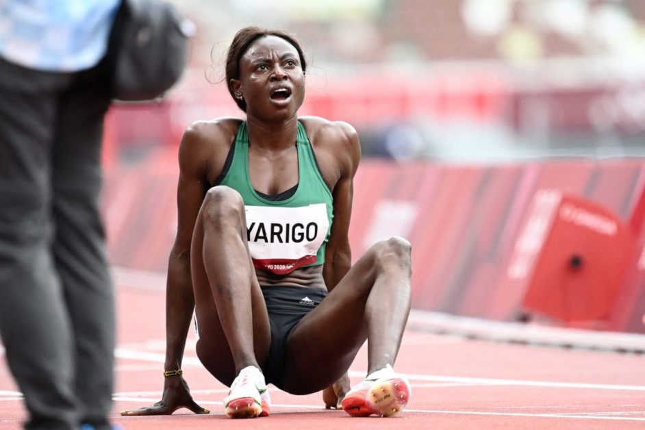 Une athlète assise sur la piste semble essoufflée ou en douleur pendant une compétition d'athlétisme