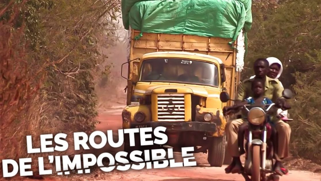 Camion chargé et plusieurs personnes à moto sur une piste poussiéreuse bordée d arbres secs avec un texte en blanc au premier plan