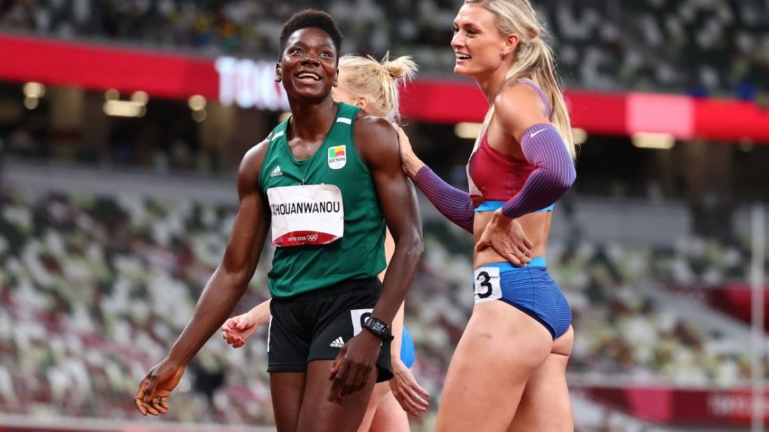 Deux athlètes féminines souriantes en tenue de compétition sur une piste dans un stade quasiment vide