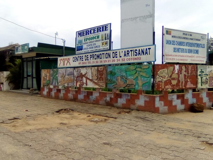Entrée d’un bâtiment avec une fresque murale colorée et plusieurs panneaux indiquant un centre de promotion de l’artisanat