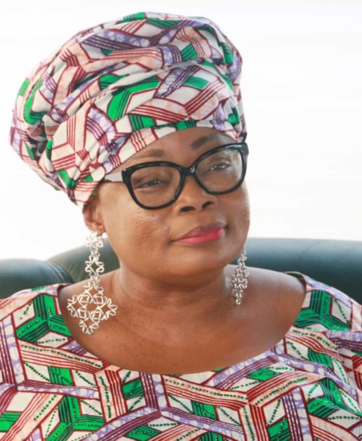 Femme portant un boubou et un foulard assorti aux motifs verts, blancs et rouges avec de grandes boucles d’oreilles argentées et des lunettes noires