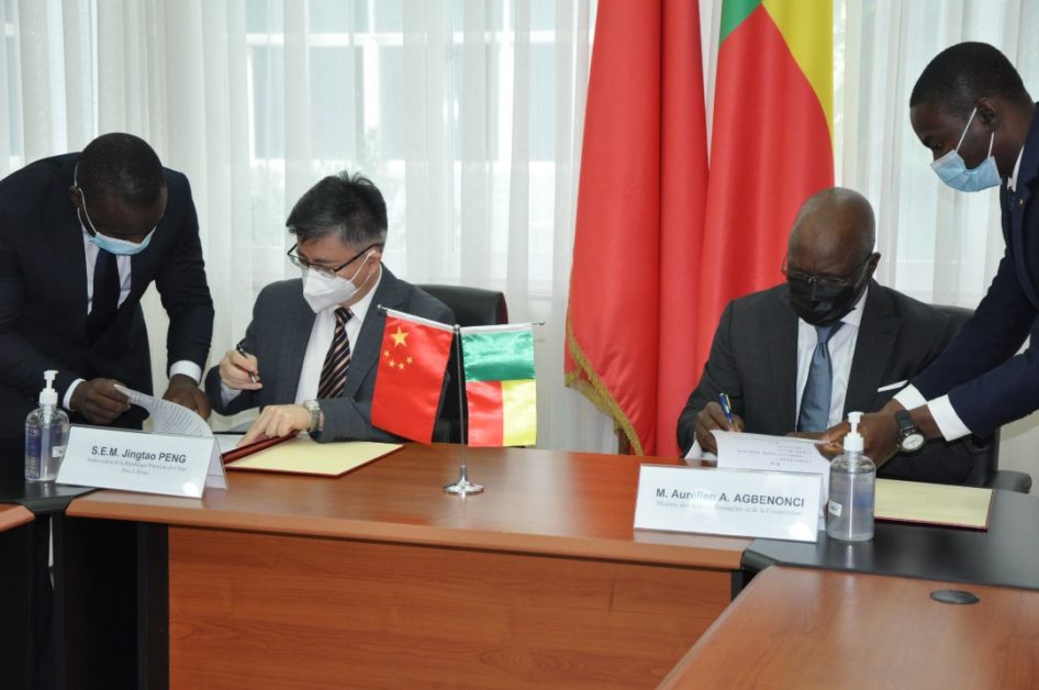 Deux hommes masqués signent des documents assis à une table avec les drapeaux de la Chine et du Bénin en arrière-plan
