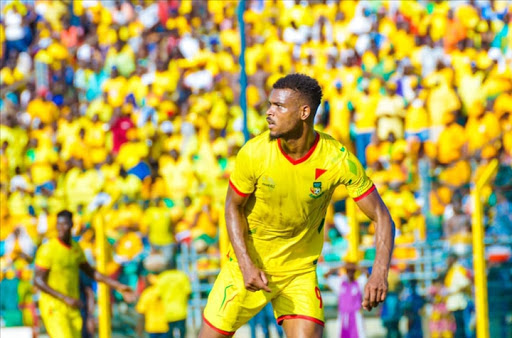 Un joueur en maillot jaune avec des détails rouges sur le terrain de football entouré d'un public également vêtu de jaune