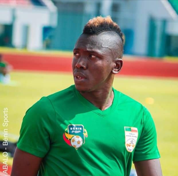 Un joueur de football en maillot vert regarde sur le côté sur un terrain extérieur.