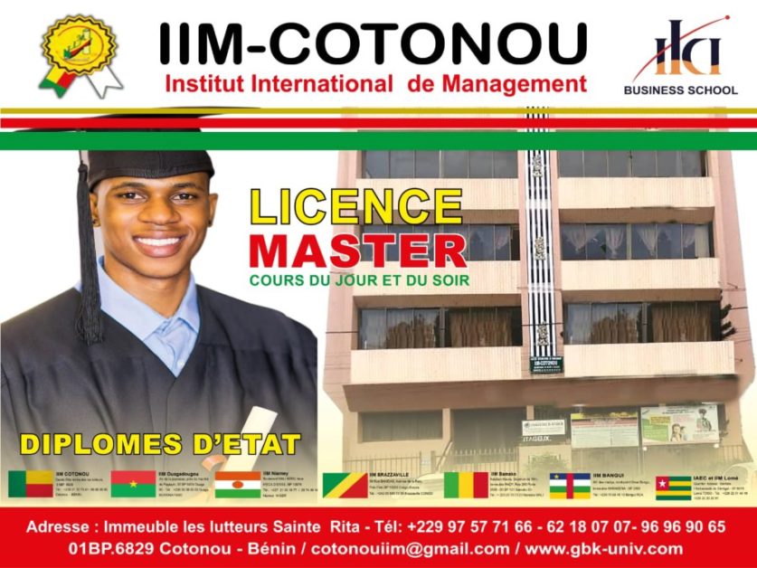Jeune diplômé en toge et à la coiffe souriant à côté d’un bâtiment abritant une école de management international