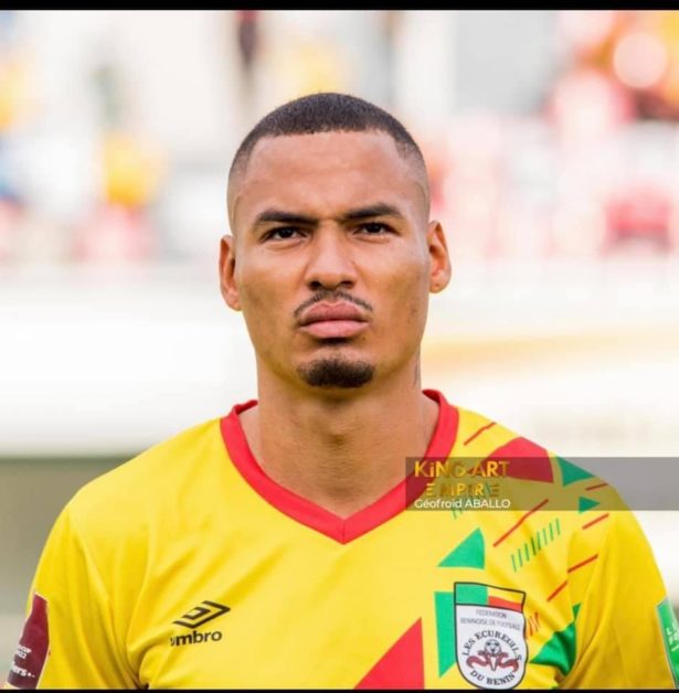 Homme en maillot jaune vif orné de rouge et vert, regard sérieux face à l’objectif sur un fond flou de stade